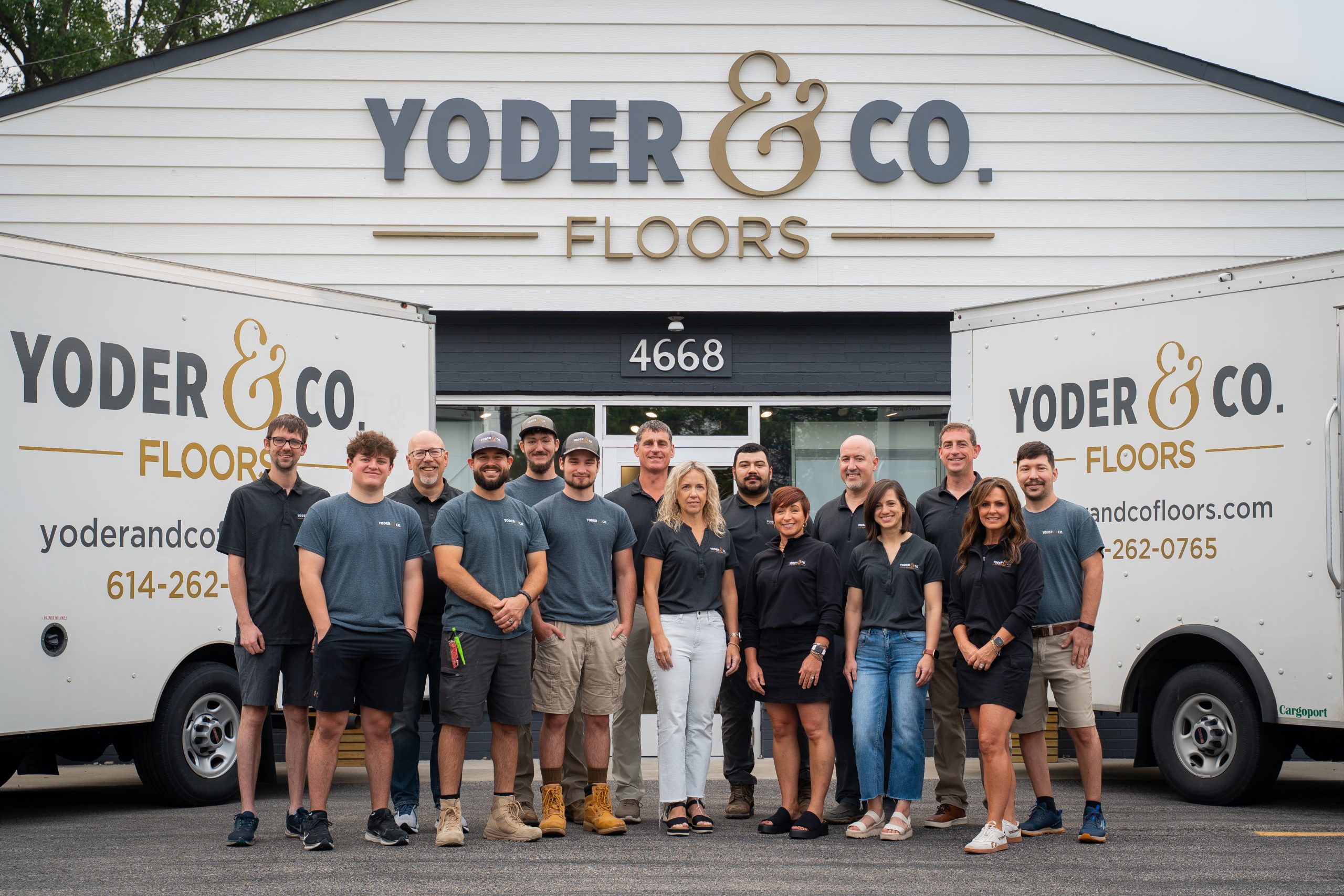 The Yoder & Co. Floors team standing together in front of their showroom entrance, with two company vans visible on either side